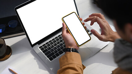 Over shoulder closeup view of man working with laptop computer and using mobile phone.