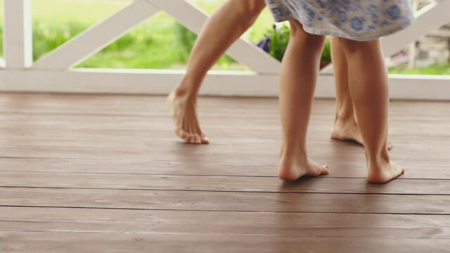Mom and daughter having fun while circling barefoot on a wooden terrace