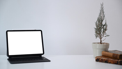 Minimal workplace with computer tablet, plant and books on white table. Blank screen for products display montage.