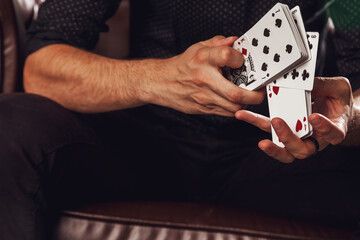 Clever hands of magician on black background. Portrait of young man with gambling cards. Handsome guy shows tricks with card on chair. Concept of entertainment and Hobbies. Copy space for site