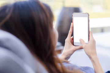 A woman shopping online on her sofa at home with a smartphone using and tap the screen to verify the identity. Concept about business. over shoulder shot