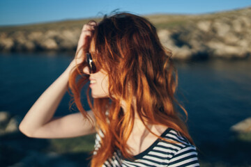 portraits of a red-haired traveler near the river in the mountains blue sky Summer sun adventure
