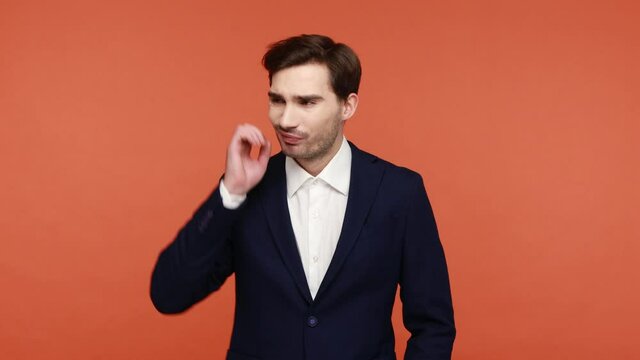 Hmm, need to think. Frustrated confused bearded guy in official suit scratching head, holding chin, contemplates how to solve problem, has doubts. Indoor studio shot isolated on orange background.