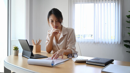 Young woman accountant analizing business data and working with computer tablet at office desk.