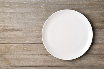 Flat lay of empty white plate on wooden table.