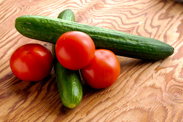 two cucumbers and three tomatoes on a wooden surface