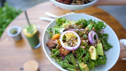 Hands presenting two vegan meals options of buddha bowl and a salad gto the camera. 