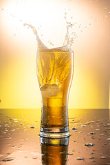 splash from a piece of ice in a glass with beer on a yellow background