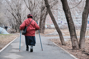An elderly woman is doing Nordic walking. Goes through the park.