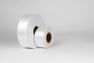 side view set of two coils of wide white satin ribbons for tags or decor, isolated on a white, gray background.