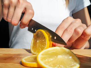 Woman cutting lemon on wooden board. Detox water with mint and lemon. Refreshing summer drink. Wellness, diet, healthy eating concept