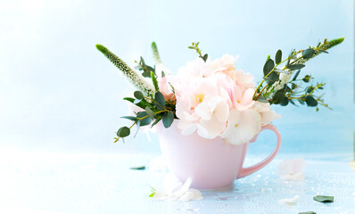 A pink cup filled with flowers: hydrangea, veronica, eucolyptus sprigs.