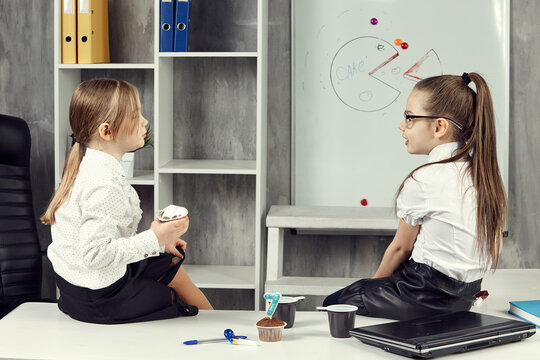 Little girls in images of office workers sit on a table and chat. Business kids chat while sitting on the table. the concept of children in the office.