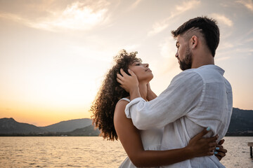 Romantic scene of bearded macho man holding head of his beautiful curly African-American woman in his hands looking into her eyes. Sentimental scene of young couple in love at sunset in nature