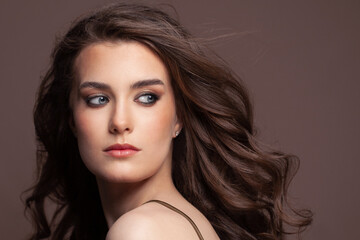 Fototapeta premium Portrait of attractive young woman with blowing long perfect dark hair on brown background