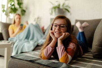 Obraz premium Photo of little girl, laying on stomach, chilling and relaxing while mom is using a cellphone.