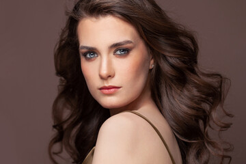 Fototapeta premium Portrait of beautiful model woman brunette with clear skin and healthy wavy hair. Pretty woman with natural makeup on brown
