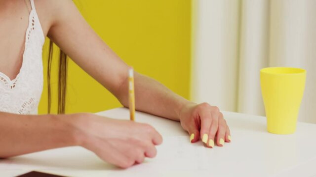 Young intelligent woman, student in glasses, is sitting at desk and making notes, getting ready to exam, trying to organise her thoughts and ideas, looks focused and confident, close up.