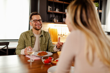 Happy young couple eating and drinking wine at home. Focus on man.