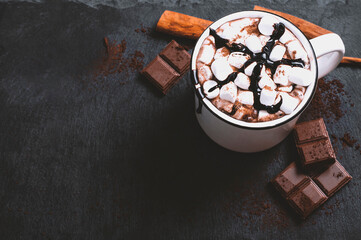 Cup of melted hot chocolate with marshmallows, cinnamon and chocolate slices on black background