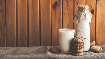 Cookie homemade breakfast with bottle and glass milk a tablecloth on a brown wooden background. Fresh healthy milk with cookies chip