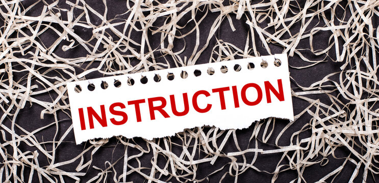 A white sheet of paper with the text INSTRUCTION lies on white shavings on a dark background.