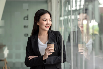 Young Asian businesswoman resting from work holding a coffee mug at the glass office.
