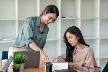 Obraz premium Two young Asian woman on brainstorming ideas together using a tablet at the office.