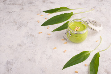 Pesto made from wild garlic, pine nuts and feta cheese in a glass, with fresh leaves on a textured background, empty space for text