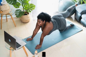 Young African curvy woman doing pilates virtual fitness class with laptop at home - Sport wellness...