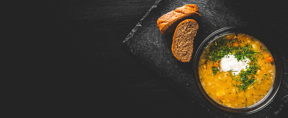 Soup with pickled cucumbers and pearl barley in black bowl on black wooden table background