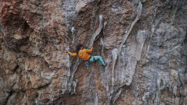 back view of strong skillful man rock climber climbs overhanging tough route with rock tufa, making very hard moves, trying to grip handhold on colonet and falling. climbing outdoors in Turkey