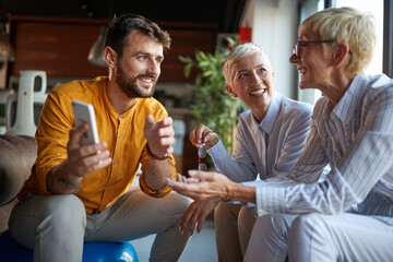 A young male businessman is chatting with his elderly female colleagues while they take a break at workplace. Business, office, job