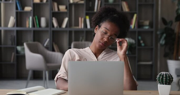 Unhappy stressed young african american woman taking off eyeglasses, suffering from blurred eyesight or pain due to long overtime computer work, feeling exhausted at office, overwork deadline concept.