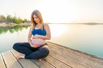 Portrait of a young happy pregnant woman sitting on a jetty during a beautiful sunset