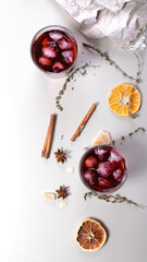 Obraz na płótnie Canvas Cherry wine cold cocktail. Alcoholic beverage banner format. Dry oranges, cinnamon sticks, oregano, anise and dried ginger. Light background. Vertical shot