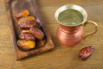 Ramadan iftar food, delicious date fruits on wooden plate and drinking water in a copper mug.  