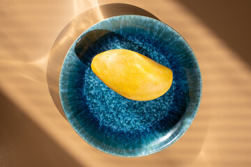 Yellow mango on blue plate shining in sunny rays. Overhead flatlay view