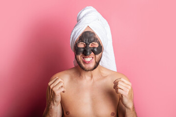 joyful young man with a cosmetic mask on his face, with closed eyes on a pink background