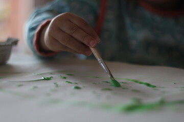 kid painting with brush on blank sheet with green paint