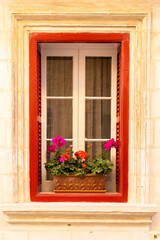 Fototapeta na wymiar Red window with geraniums colorful flowers in clay pot