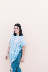 Teen girl in a tie dye shirt on a flat orange wall looking at camera