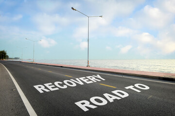 Road to recovery written on asphalt road with marking line for given direction and sea landscape