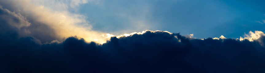 Dark storm clouds illuminated by the bright evening sun, panorama