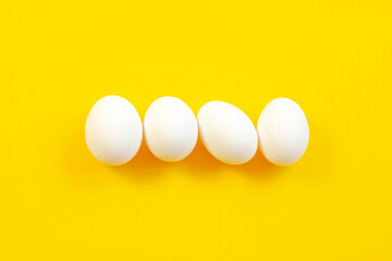 White eggs on a yellow background in the center, top view, copy space. Raw eggs on a yellow background, copy space, top view. White egg on a yellow background, top view. Design, minimalism, fine art.