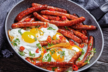 sausages with fried eggs in a pan, top view