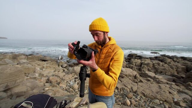 Man is looking at the camera screen on getting prepared for taking pictures of beautiful marine landscape. Seaside