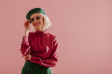 Spring fashion concept: happy smiling elegant woman wearing stylish green beret, sunglasses, satin blouse, posing on pink background. Copy, empty space for text
