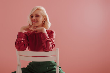 Elegant happy smiling blonde woman wearing stylish satin blouse, green torusers, posing on pink background. Copy, empty space for text