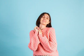 Young brunette in warm pink sweater isolated on blue background happy positive hugging herself smile